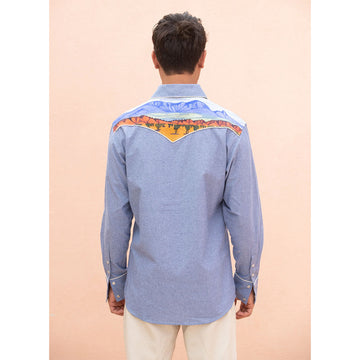 Man wearing a blue denim shirt with Indigenous designs on the shoulders on a beige background.