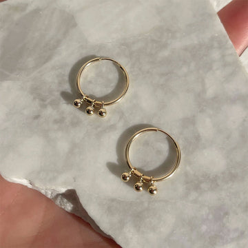 Gold hoop earrings with small spherical charms on a marble surface.