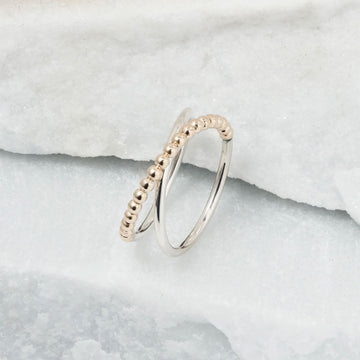 A ring with a cross over design and gold beads.