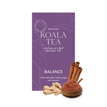 A purple box with white writing, loose tea in a wooden bowl, cinnamon sticks and a ginger root.