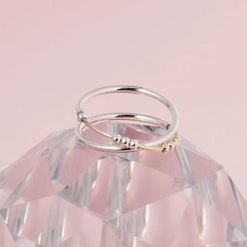 A silver ring with a cross over design and silver and gold beads.