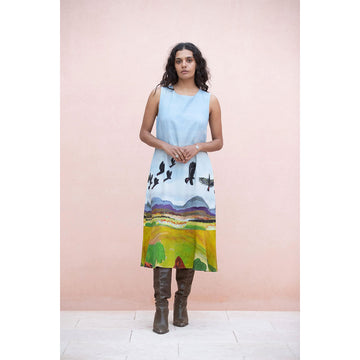 Woman wearing a sleeveless dress with a colorful landscape design with birds flying against a pink background.