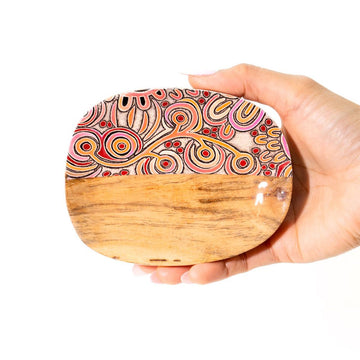 Hand holding a wooden trinket dish with a colorful pattern on a white background.