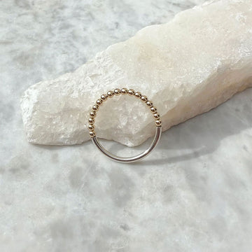 Gold beaded ring on a textured white surface.