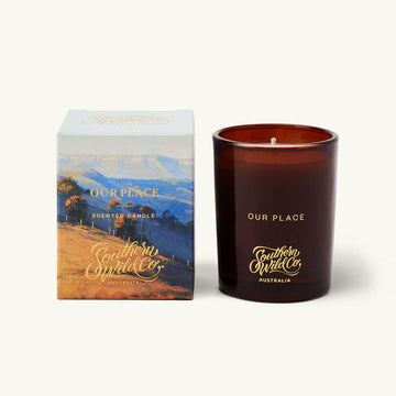 Brown candle with 'Our Place' branding next to its packaging on a white background.