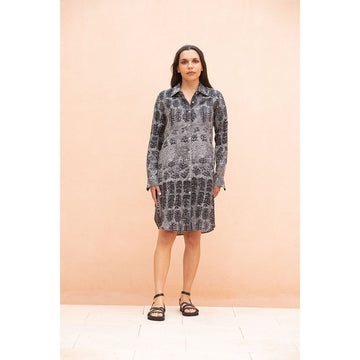 Woman wearing a patterned dress against a peach-colored wall.