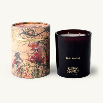 Black candle labeled 'Bush Magic' next to decorative box on a white background.