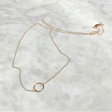 Gold necklace with a circular pendant on a light gray background.