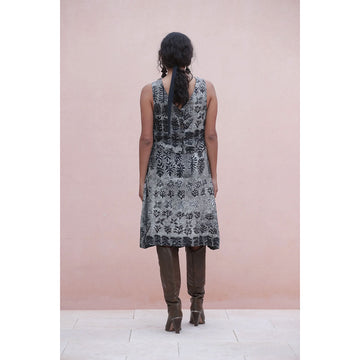 Woman wearing a patterned dress and high boots against a pink wall.