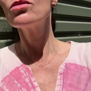 Gold necklace with a circular pendant on a light gray background.