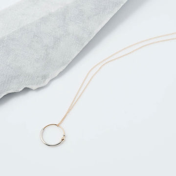 Gold necklace with a circular pendant on a light gray fabric background