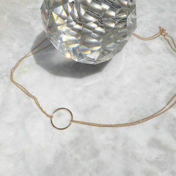 Gold necklace with a small circular pendant on a textured white surface.