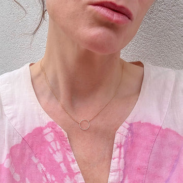 Gold necklace with a small circular pendant on a textured white surface.