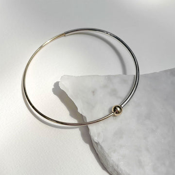 Gold bracelet with a small gold bead on a white marble surface.