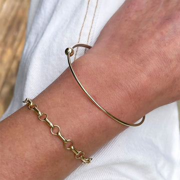 Gold bracelet with a small gold bead on a white marble surface.