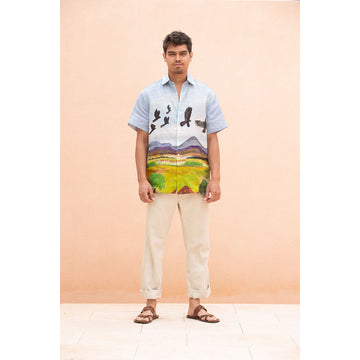 Man wearing a colorful shirt with a landscape design against a peach background.