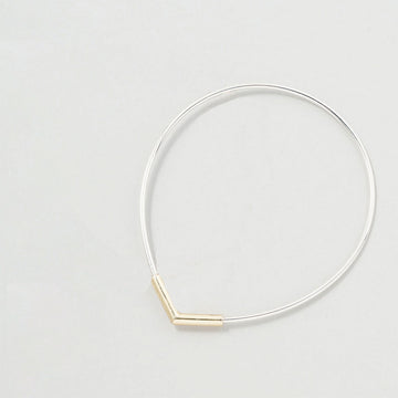Thin silver bangle with a gold bar pendant on a light gray background.