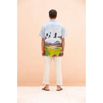 Man wearing a colorful shirt with a landscape design against a peach background.