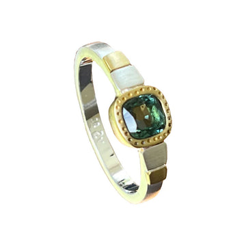 A silver ring with gold accents on the band and a green topaz stone in a gold bezel in the middle.