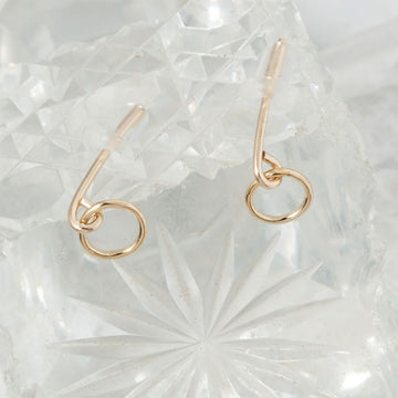 Gold stud earrings with a small circle on a textured white surface.