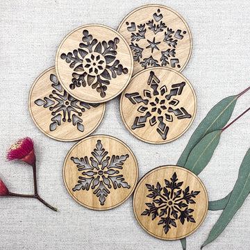 Wooden coasters with snowflake designs on a textured surface with floral elements.