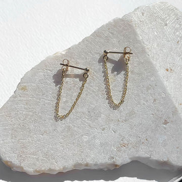 Gold chain earrings on a light stone surface.