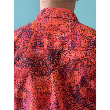 Front view of a model wearing a men's shirt printed with artwork by Andrea Adamson in shades of red and brown.