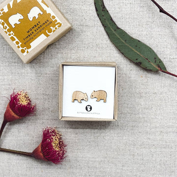 Wombat earrings in a box with flowers and leaves on a textured surface.