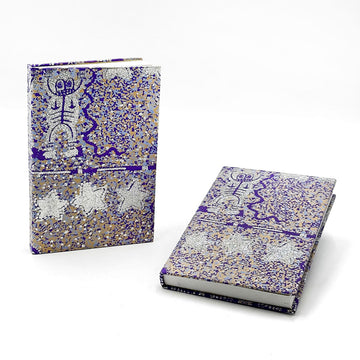 A notebook pictured twice, one standing up and one laying down. They are printed with artwork by Cedric Varcoe with glitter.