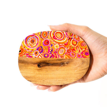 Hand holding a wooden trinket dish with a colorful circular pattern printed on half of the dish.