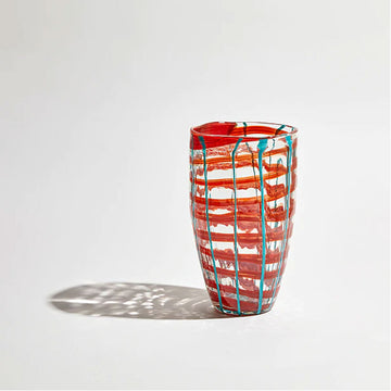 A tall cylinder glass vase with tapers out at the top and painted with a red and green checkered print.