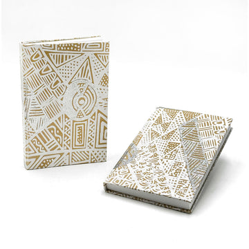 A notebook pictured twice, one is lying down and the other is standing up. They are printed with artwork by Simplicia Tipungwuti with glitter.