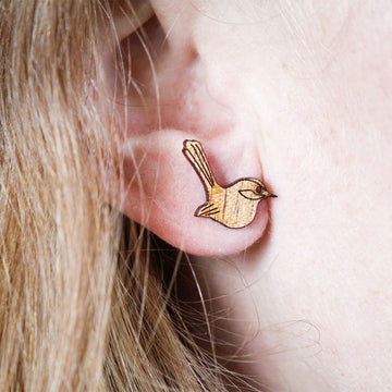 A pair of wooden fairy wren earrings in a box surrounded by leaves and flowers.