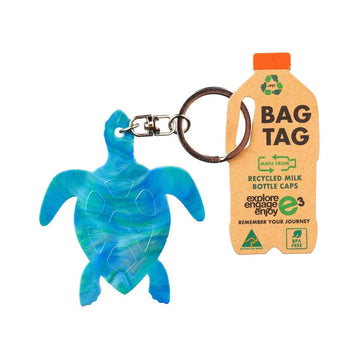 Blue turtle-shaped keychain and recycled milk bottle cap bag tag on a white background.