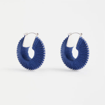 A pair of hoop earrings with cobalt blue thread around the edges.