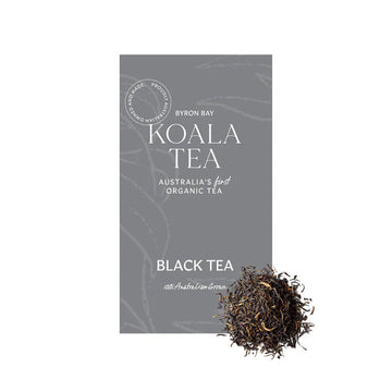 A grey box of tea with white writing sitting behind black loose leaf tea.