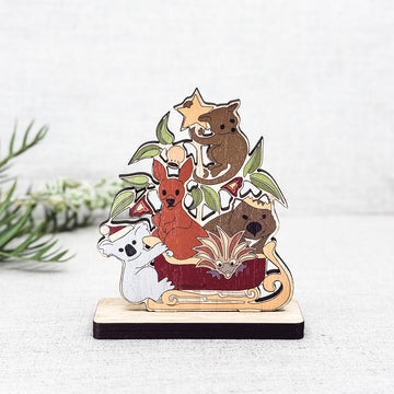 Wooden ornament of Australian animals riding a sleigh on a white background.