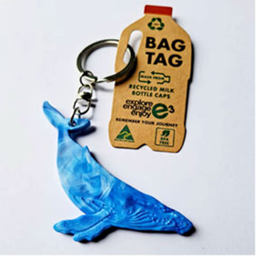 Blue whale-shaped keychain attached to a recycled milk bottle cap keyring on a white background.