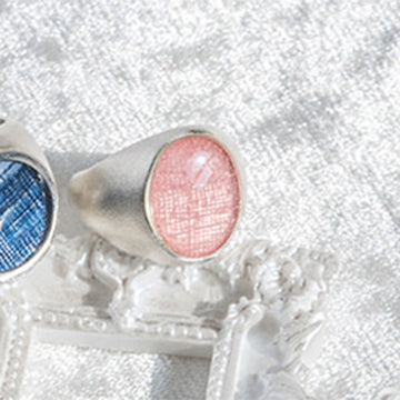 Close-up of a silver ring with pink gemstone on a textured white background