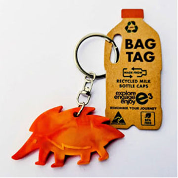 Orange echidna-shaped keychain attached to a recycled milk bottle cap bag tag on a white background