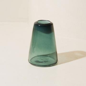 Green glass vase on a white surface with a light background.