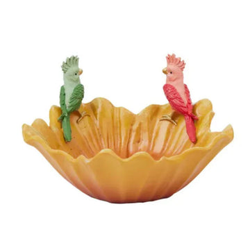 A flower shaped bowl in yellow with a green and a pink bird sitting on top.