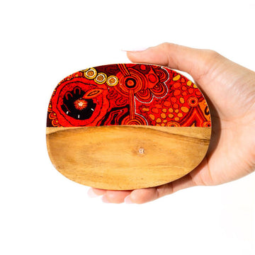 Hand holding a wooden trinket tray with a colorful design on half the tray on a white background.