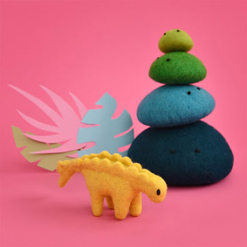 A yellow stegosaurus made from felt standing next to a stack of blue and green felt rocks.