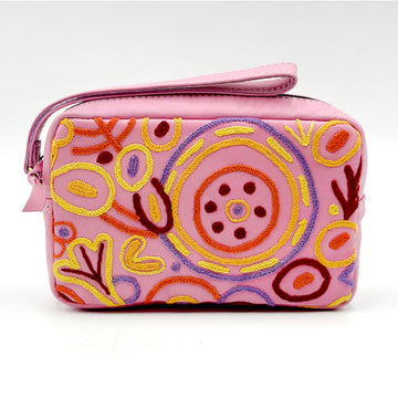 A pink velvet rectangle toiletry bag embroidered with artwork by Cedric Varcoe. There is a matching pink wrist strap on top.