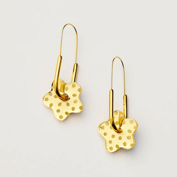 Gold earrings shaped like flowers on a hoop with a polka dot design on a light gray background.