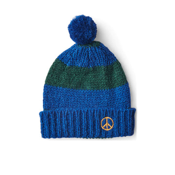 A knitted blue beanie with a green horizontal stripe. There is a blue pom pom on top and a yellow peace symbol on the cuff.