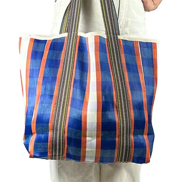 Close up of a model holding an orange and blue striped tote bag against their body.