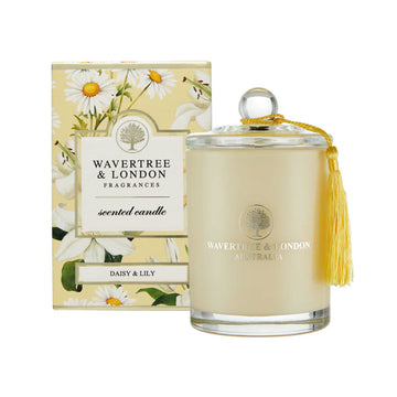 A glass candle in a pale yellow next to a box illustrated with daisies and lilies. 