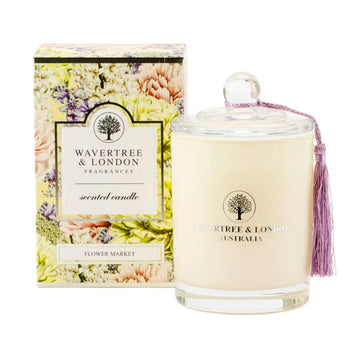 A glass candle in a light cream colour next to a box illustrated with colourful flowers.